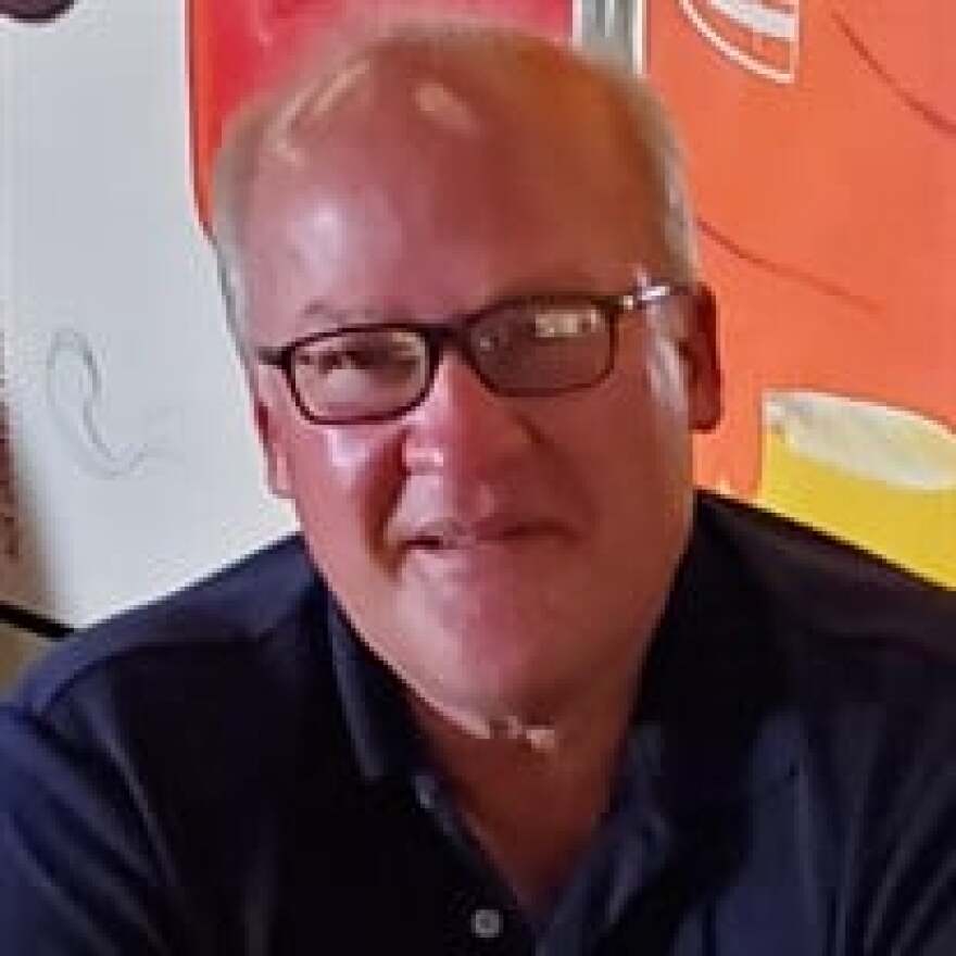 A head shot of Cheektowaga Police Chief Michael Sliwinski, wearing black glasses, in a dark blue shirt in front of multicolored background