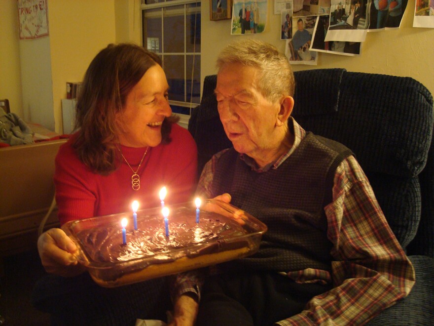 Susan Cerulean holding a cake with lit candles sitting next to older man