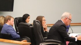 Five people sit at a courtroom desk facing away from the camera. 