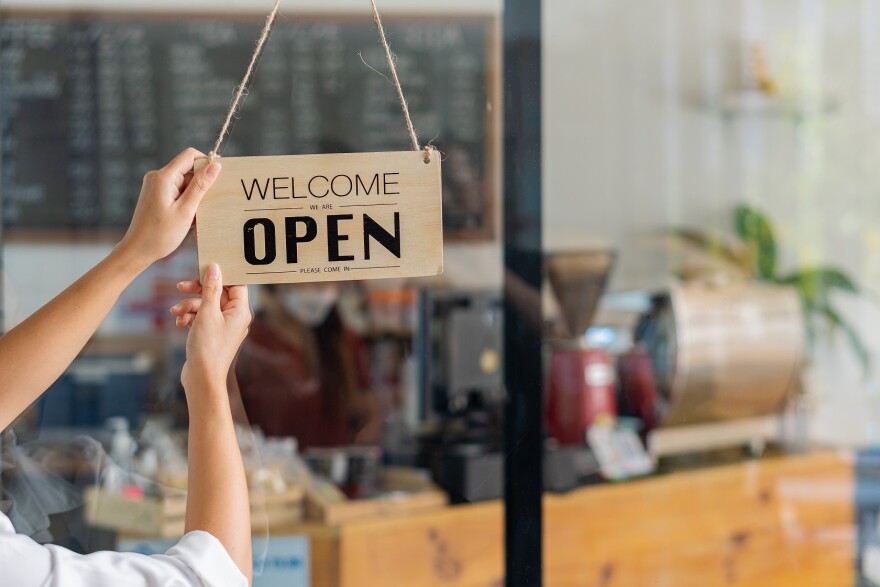 Barista female hand holding open sign in coffee shop that says Welcome