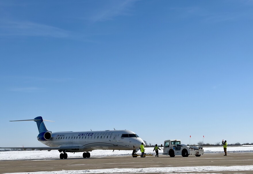 A United Airlines jet is readied for take off by three members of the ground crew who are wearing neon yellow. 
