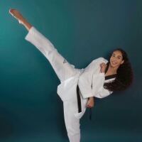 Taekwondo athlete Aliyah Shipman poses for a photo in her uniform with a green photo background behind her