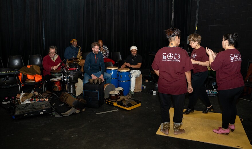 Dancers dance in front of a band in a small studio