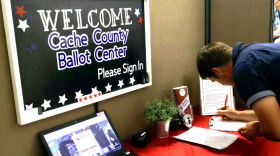 Visitor Chris Barnes signs in to the ballot center. Anyone entering the building must record their name, as well as the date and time of their visit. The sign above him reads "Welcome. Cache County Ballot Center. Please sign in."