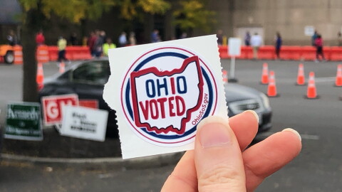 A hand holds an Ohio Voted sticker outside a polling site