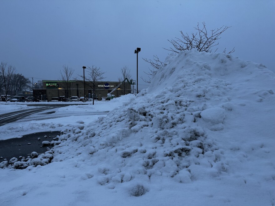 Snow piles more than 10 feet high fill a shopping center parking lot in Elkhart after the weekend storm, as crews work to clear heavy, wet snow from the area.