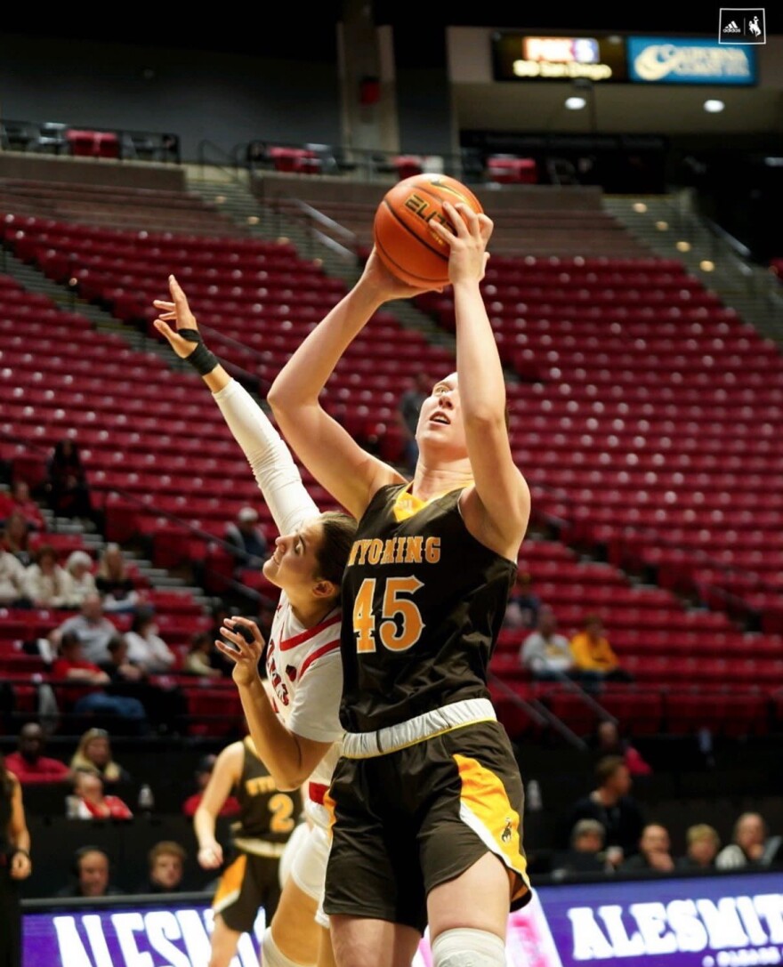 A University of Wyoming Cowgirl basketball player lines up for a shot while a rival team member tries to block.