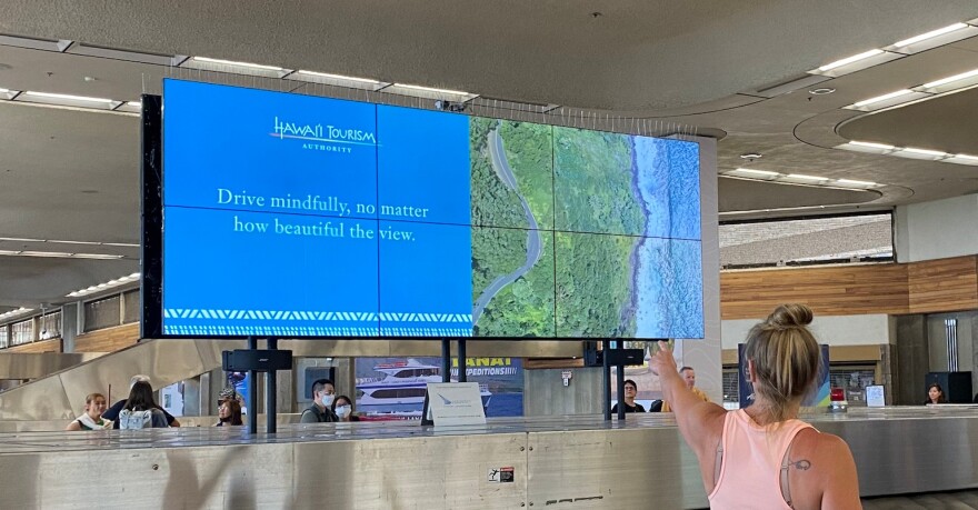 FILE - A traveler points to a Hawaiʻi Tourism Authority message board at Kahului Airport on Maui.