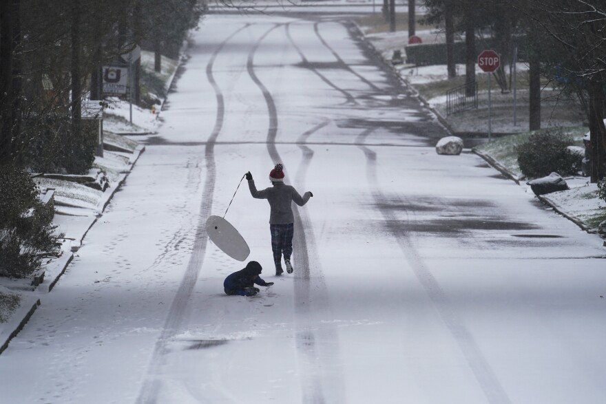 Child running down snowy road with boogie board and dog.