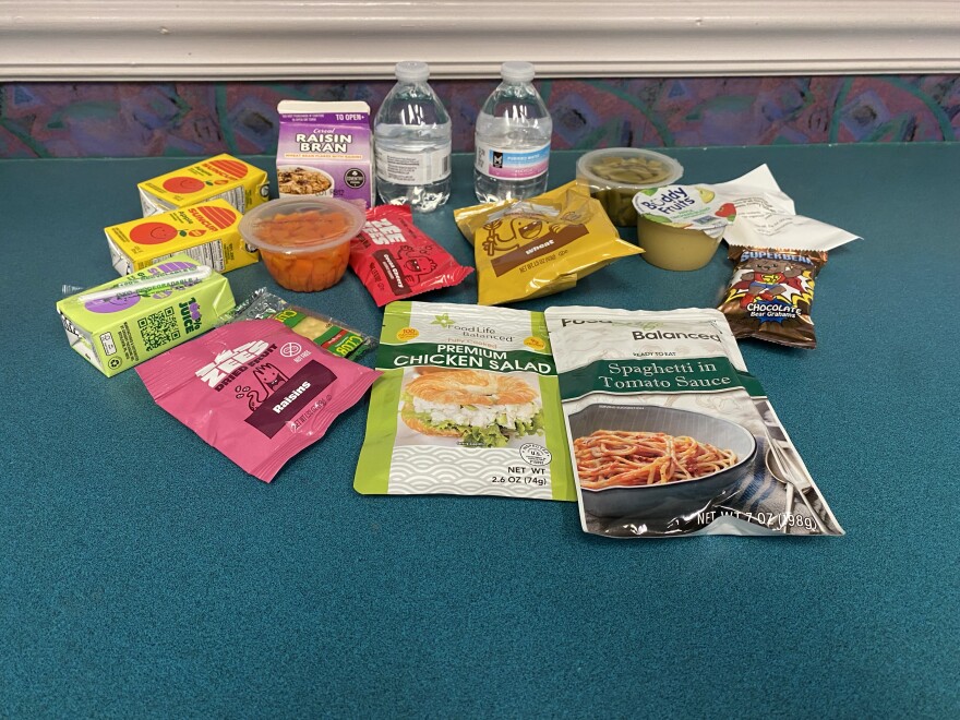 Packets of food including chicken salad, spaghetti in tomato sauce, juice boxes, water, cereal, apple sauce and non-perishable snacks are sprawled on the counter.
