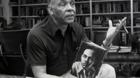 Ralph Ellison in conversation, holding a cigar and a copy of his novel