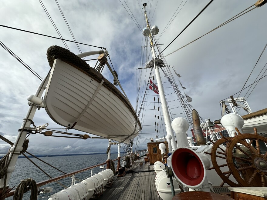 A life boat is suspended above the deck of the Statsraad Lehmkuhl on a partly sunny day.