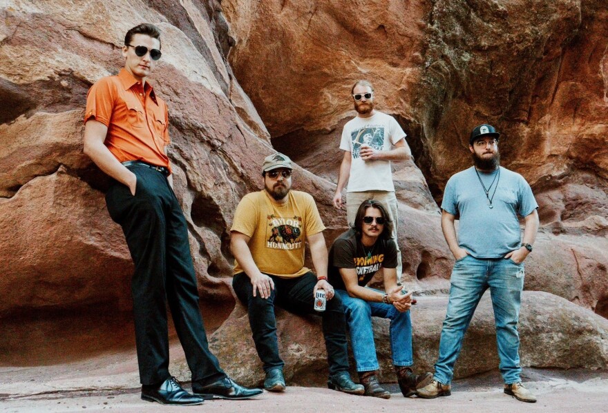 A group of men standing in front of red clay rocks. 