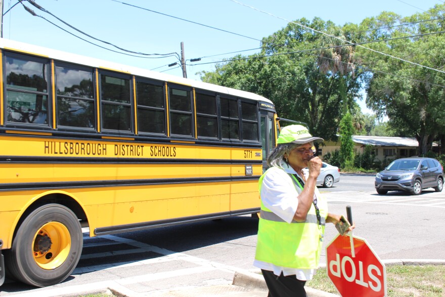 woman crossing guard holds stop sign in front of school bus