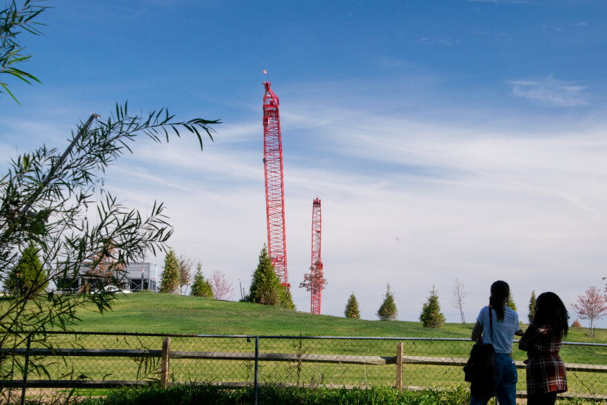 Two people stand at the edge of a backyard, looking over a chain-link fence into the Google Project Zodiac construction site.