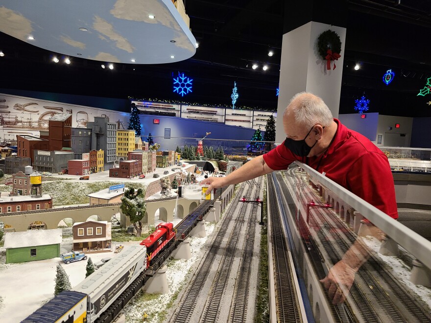 man in red shirt reaches into a model train display to add powdered fake snow