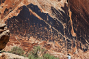 Photo of a rock wall at Bears Ears National Monument that's covered in ancient drawings by Native tribes. A person can be seen taking a picture of it in the corner.