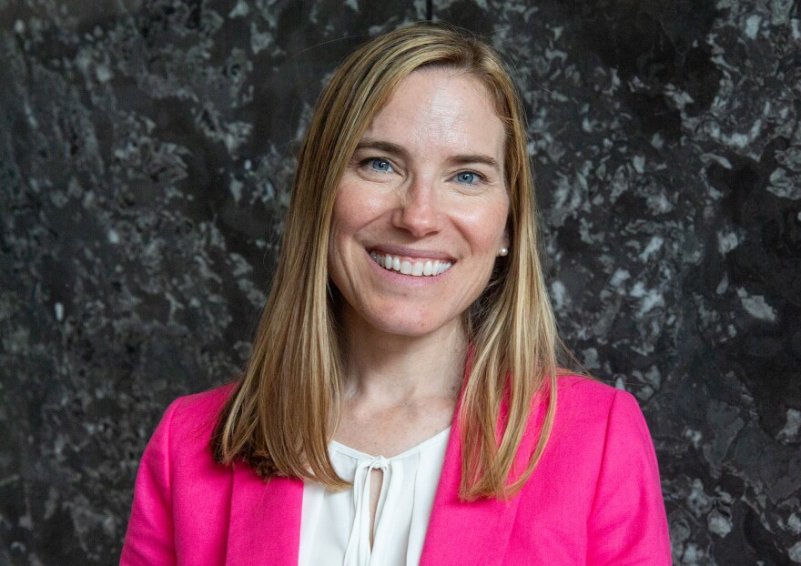 A photo of a blonde white woman in a hot pink blazer against a grey background