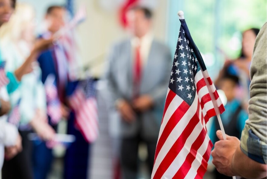 Blurred image of man in suit speaking to a group of people with someone in foreground holding American flag