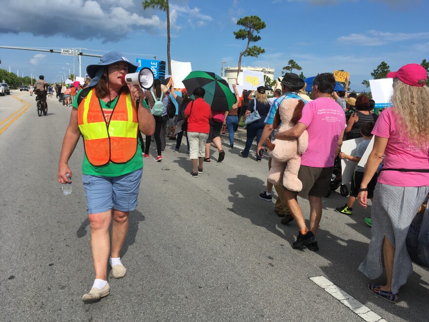 An official guides protesters down 288th Street, in Homestead, Fl., telling them to stay on the right side of the road