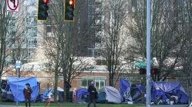 Pedestrians walk past tents used by people lacking housing at Denny Park near the Space Needle in Seattle in March 2021. A judge on Friday struck a Seattle measure on homelessness from the November ballot even as the city remains mired in a long-term humanitarian crisis.