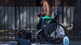 A man standing up from a wheelchair prepares to inject himself with a needle on Southampton Street in the Mass. and Cass area of Boston. (Jesse Costa/WBUR)