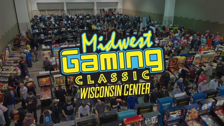 A wide shot of a convention floor with thousands of people milling around among various gaming machines, including arcade cabinets and pinball.