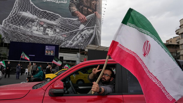 A man flashes a victory sign as he carries an Iranian flag in front of an anti-U.S. billboard depicting the American aircrafts into the Iranian armed forces fishing net with signs that read in Farsi: "The Strait of Hormuz will remain closed, The entire Persian Gulf is our hunting ground," at the Eqelab-e-Eslami, or Islamic Revolution Square in downtown Tehran, Iran, Monday, April 13, 2026.