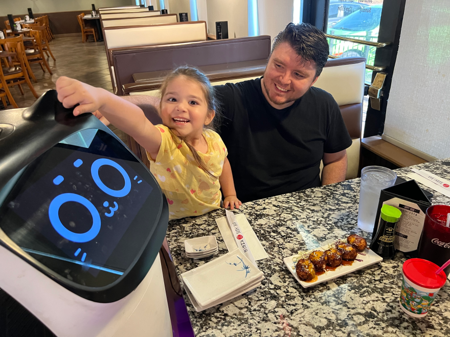 Four-year-old Emily Escalante, tickles the ears of Bella the cat robot, before eating dinner at Ninza Sushi East.