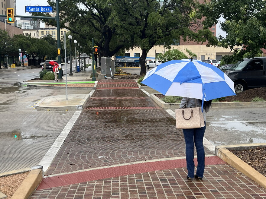A woman waits in the rain to cross a downtown street on Oct. 2, 2026.