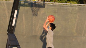 A boy wearing a mask shoots on an outdoor basketball court.