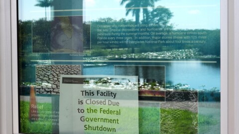 A sign alerting visitors that the Royal Palm Visitor Center is closed due to the federal government shutdown hangs in a display case reflecting the landscape, inside Florida's Everglades National Park, Wednesday, Oct. 1, 2025.  