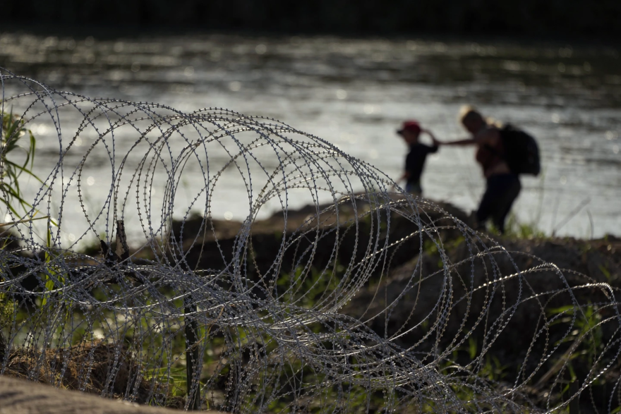 Inmigrantes en Eagle Pass, Texas, caminan cerca de las concertinas levantadas por agentes estatales que participan en la Operación Lone Star.