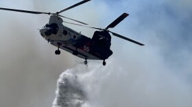 Firefighting efforts on the Sandy Fire include both ground and aerial support. Here, a helicopter drops fire retardant on May 18, 2026.