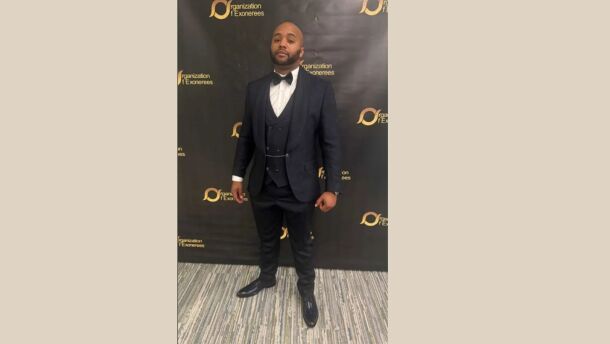 Eric Anderson stands in front of a step and repeat black background while wearing a three-piece suit