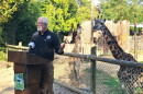 man at a podium with a giraffe behind him