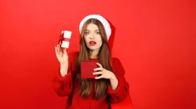 Young woman in New Year's clothes is upset with a Christmas gift, negative emotions. People on a red background.