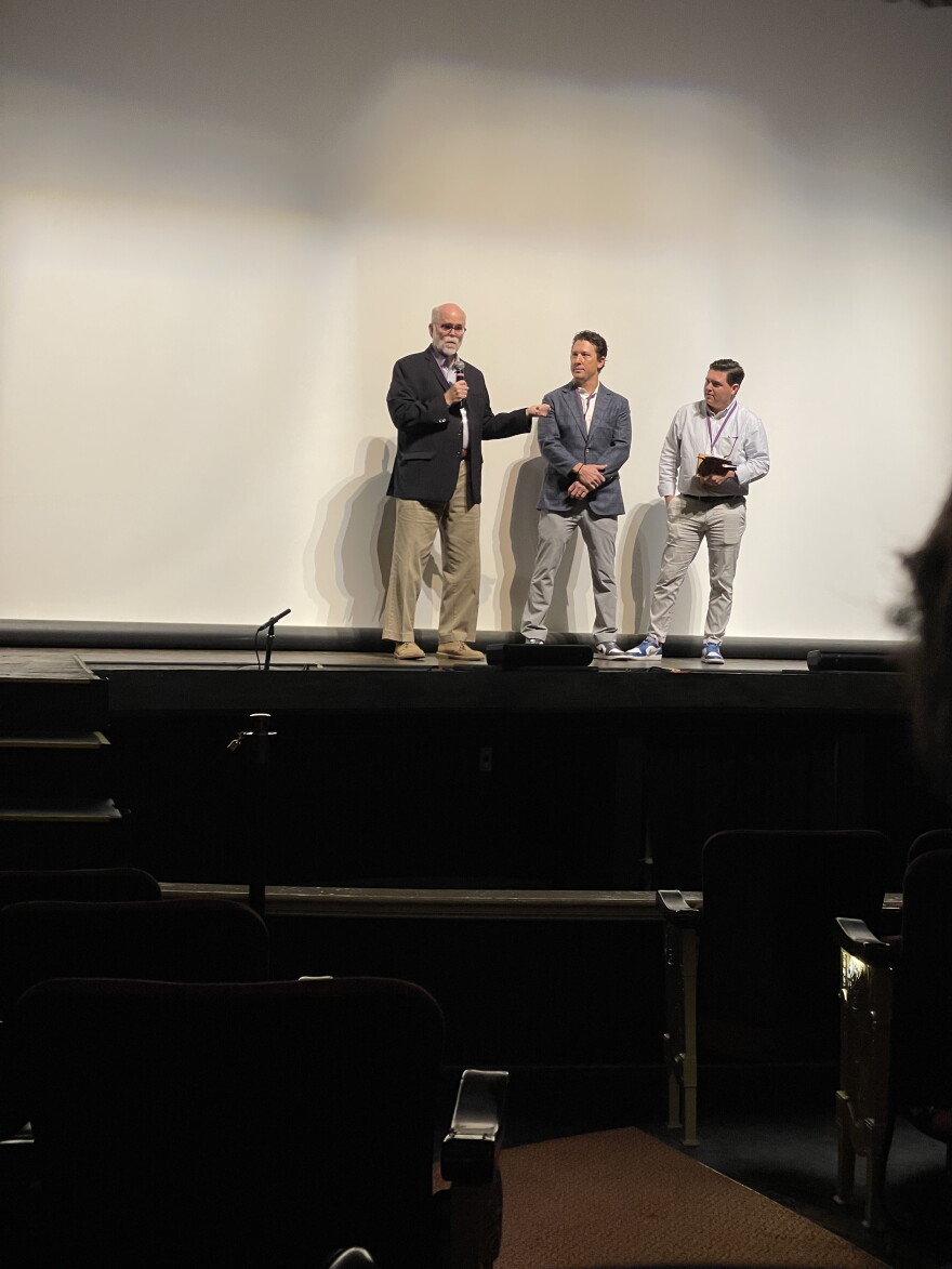Three men stand on a stage.