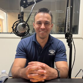 Mike Escobar smiles for a photo inside a sound booth.