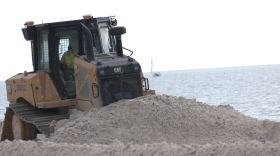 Bulldozer pushes sand across beach in Naples