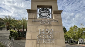 A large stone marker outside reads 'administration center' with the address. Behind are palm trees and blue sky. 
