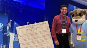 Tulsa Public Schools speech and debate teacher Micah Cash takes a picture with Ollie the Otter, a mascot at the Teacher Freedom Alliance (TFA) summer conference in July, where there was also a poster-sized Declaration of Independence from Teacher Unions sign encapsulating the organization's mission. In the background, Former Oklahoma State Superintendent Ryan Walters, now the CEO of TFA, gives a speech to a crowd of attendees during a banquet. The images used for clip art were provided by Cash.