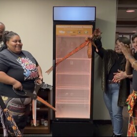 Melody McCurtis (center), Deputy Director of Metcalfe Park Community Bridges, cut the ribbon on a new community powered fridge at the organization's headquarters.
