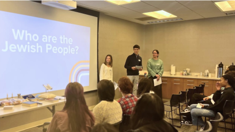 Three Jewish students speak in front of a classroom with a projection on the screen reading "who are the Jewish people?"