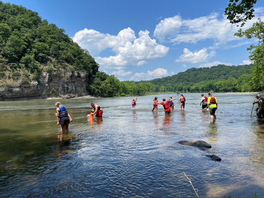 Campers wearing red and blue life vests peer into the New River. One boy is enjoying splashing in the water. 