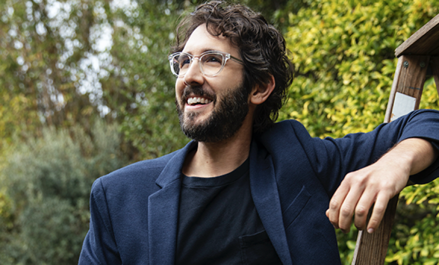 Man with brown hair and clear glasses stands outside 
