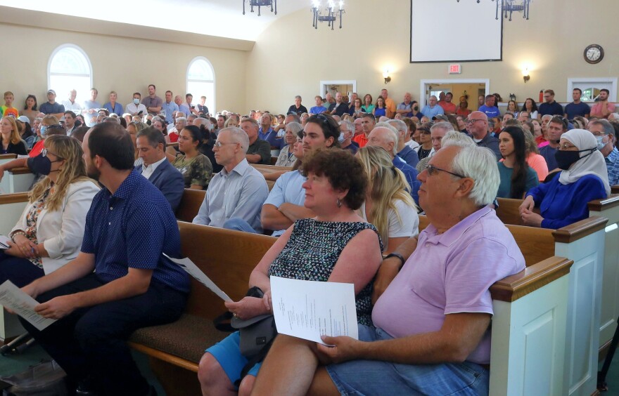 Hundreds of people fill the pews at a church during a community meeting.