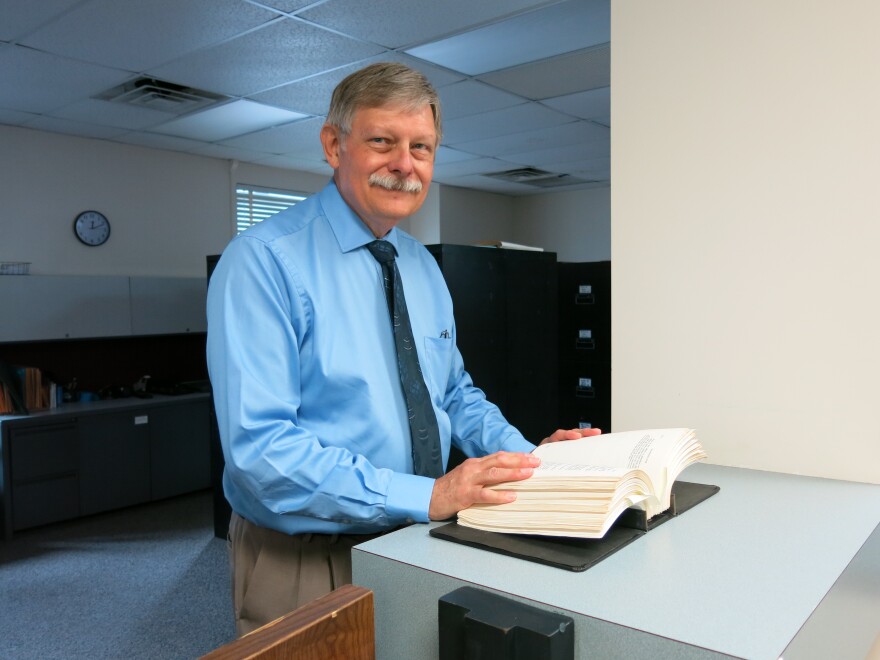 Clyde Robinson, Kalamazoo City Attorney, stands behind the counter at the City Attorney's Office in Kalamazoo City Hall. His hands are resting on the old Kalamazoo ordinances book.  