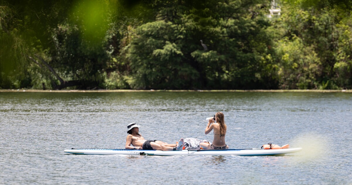 A man and woman sit on paddle boards on Lady Bird Lake. The woman is drinking water