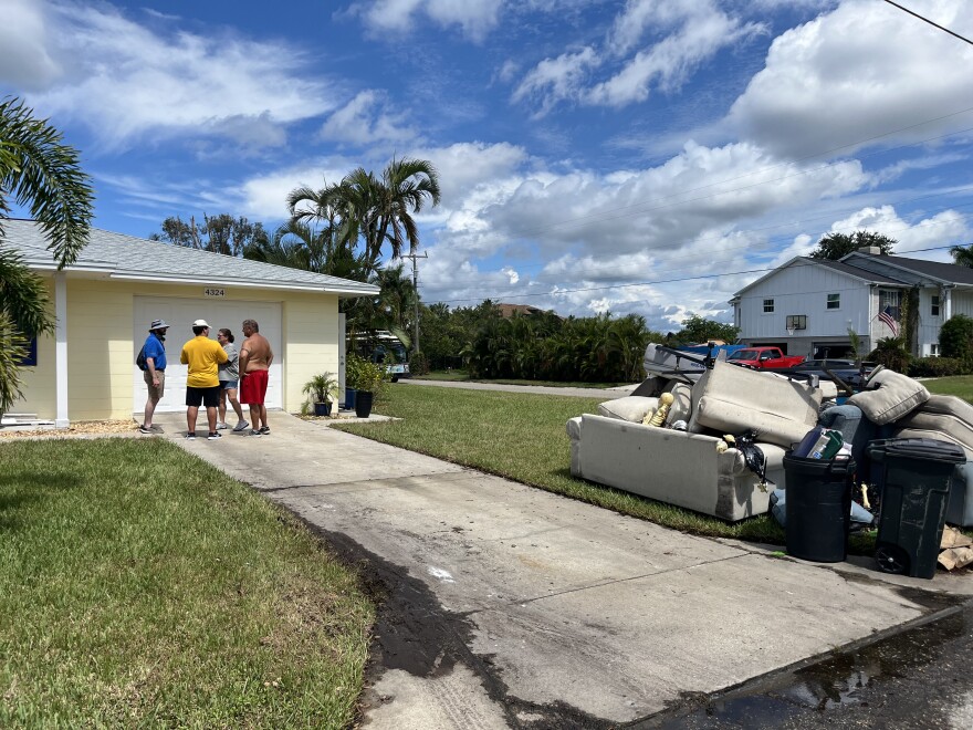Two volunteers talk to a husband and wife outside a home where a pile of furniture sits on the sidewalk.